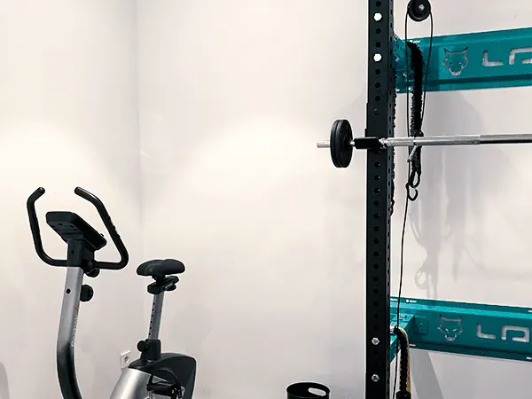 La sala de ejercicio: la jaula con la barra y los discos, y la bicicleta estática