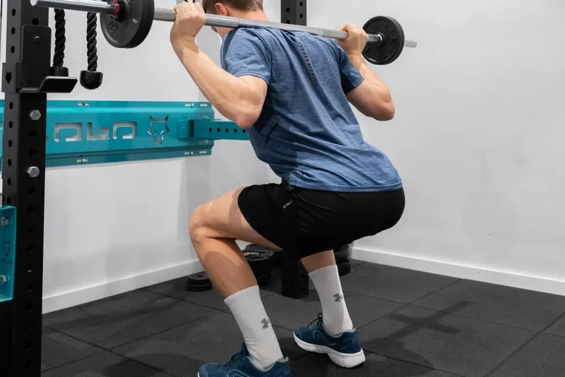 Sentadilla con barra en la jaula de la sala de ejercicio de Activefisio